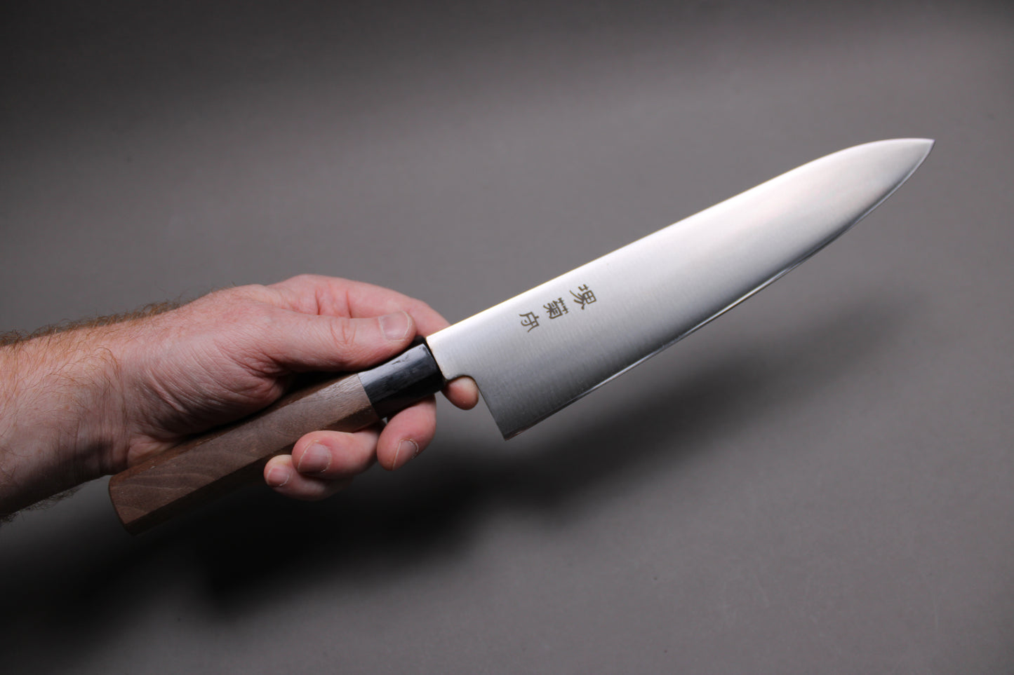 hand holding kawamura hamono 240mm gyuto with kanji blacksmith