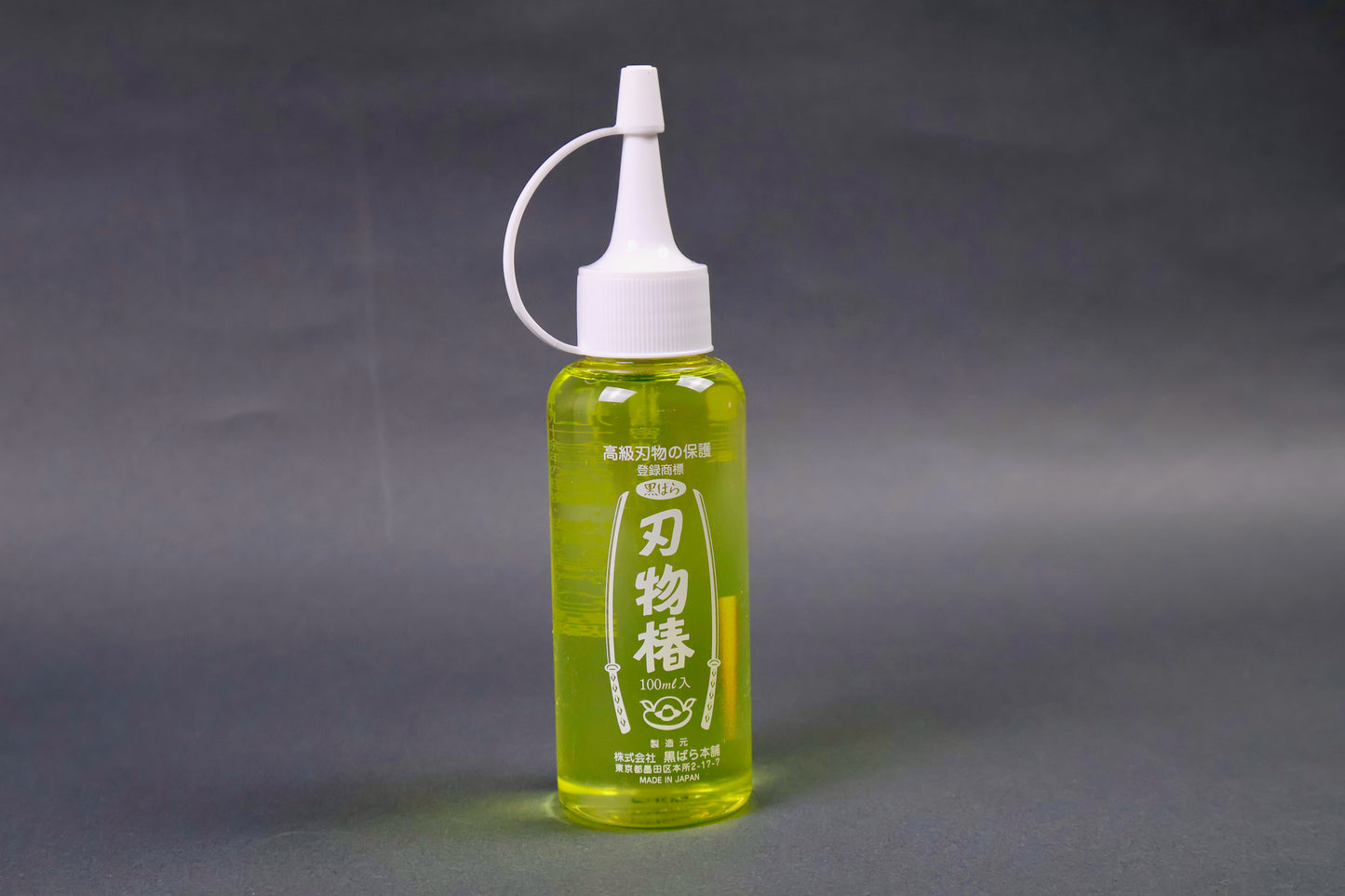 clear plastic 100ml dispenser bottle with looped white cap yellowish gold oil showing white print on container with sword animations and hiragana grey background