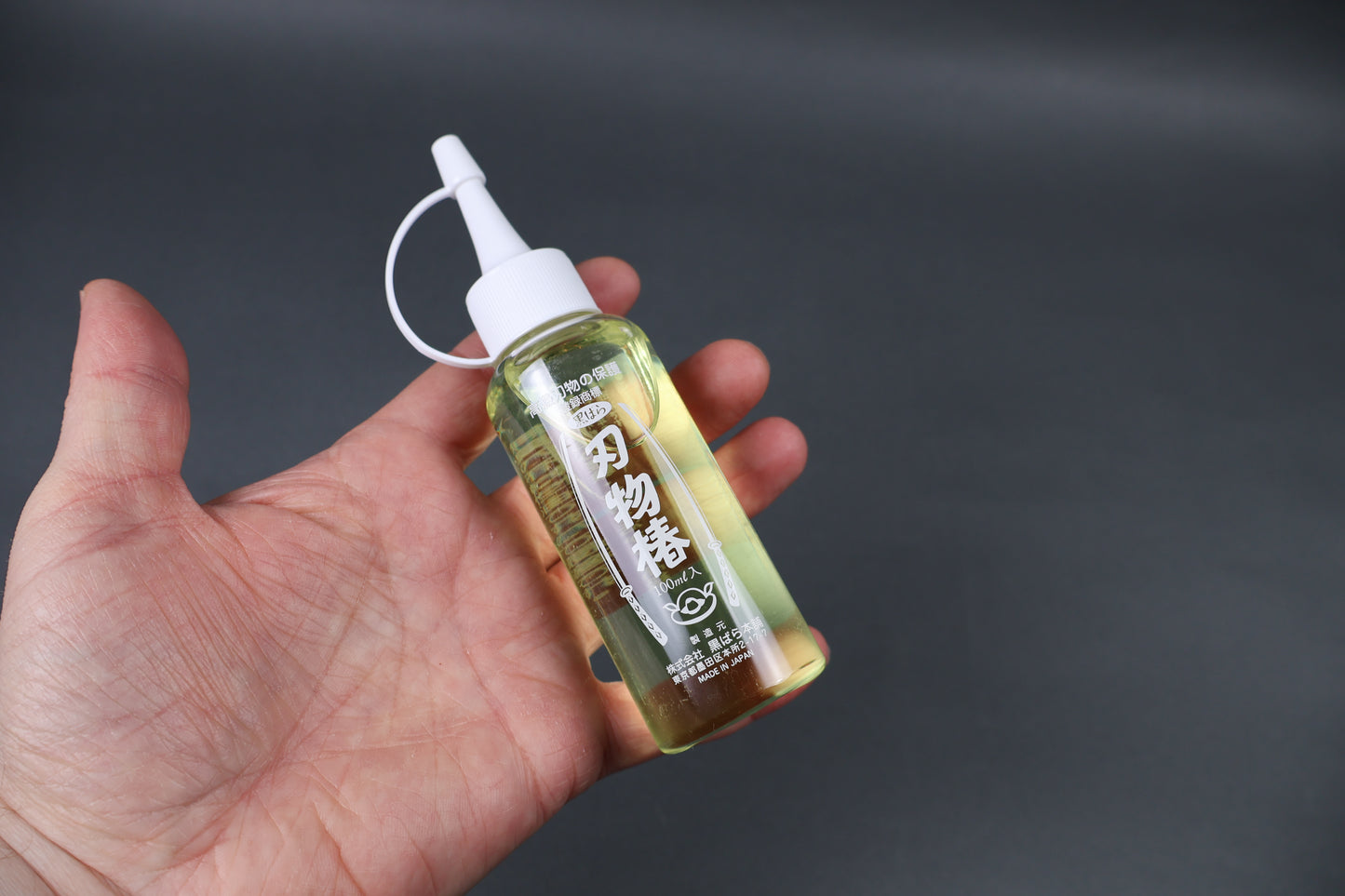 tsubaki oil used in kitchens to prevent rusting on cast iron pans kitchen knives and other kitchenware held in hand angled shot dark grey background