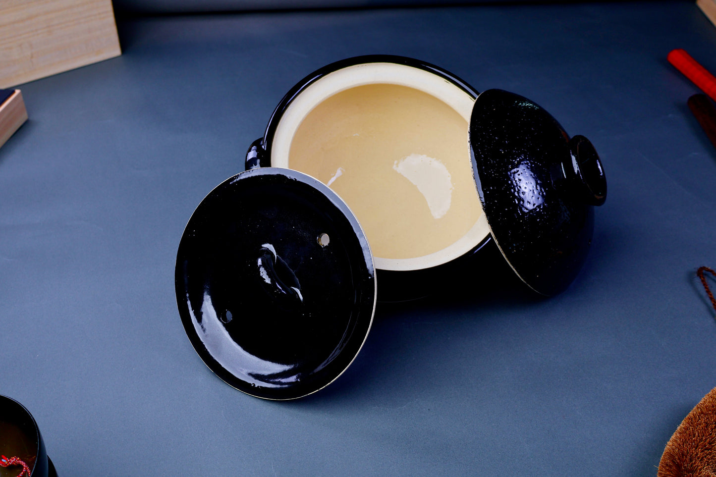black glazed and clear glazed two lidded rice cooker tilted to see clear shiny interior in grey backdrop