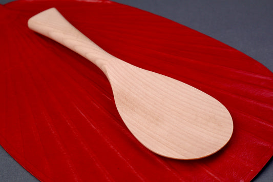 hand carved wooden rice paddle light golden brown yellowish tone of paddle atop deep red background surface