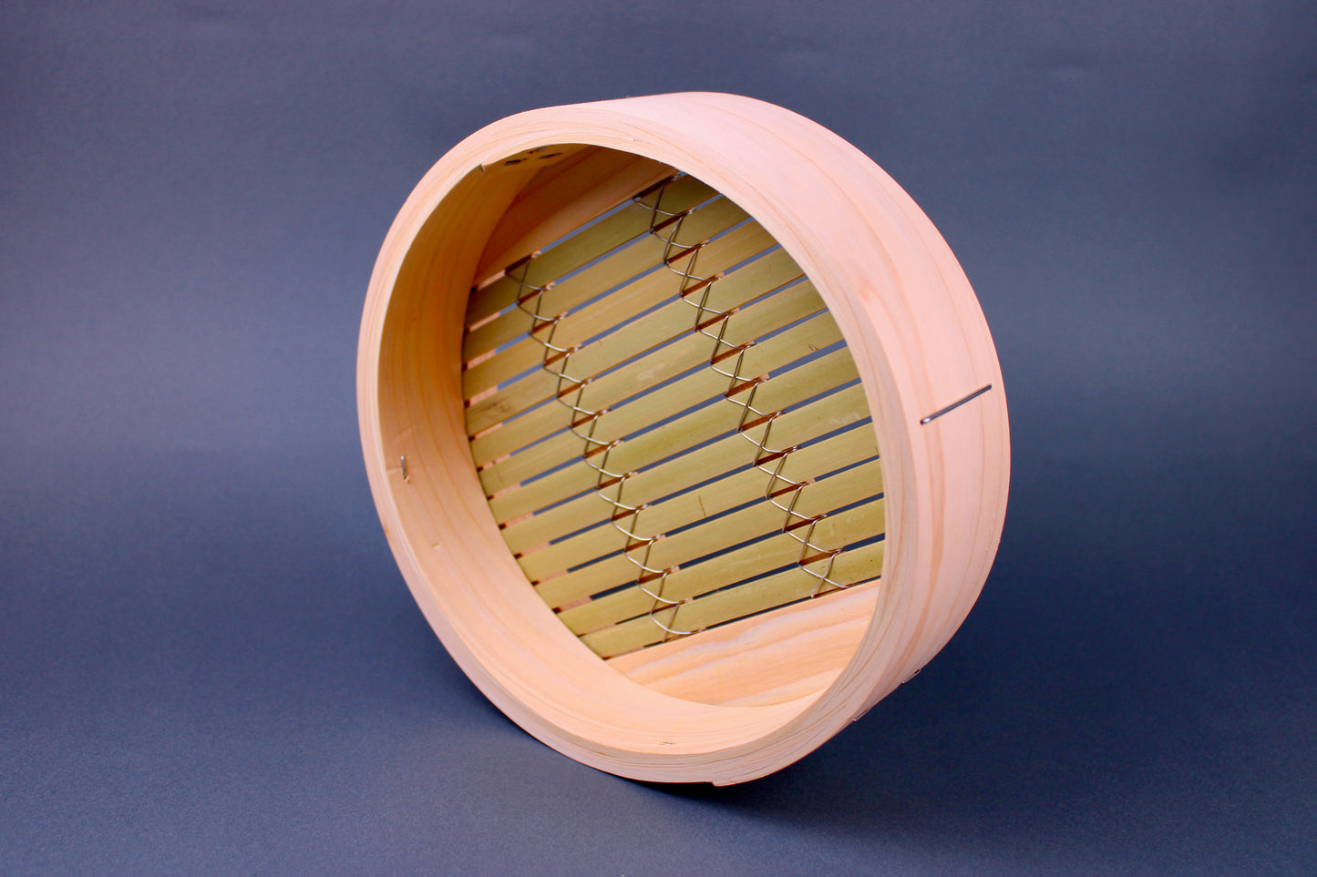 round thick hinoki wood bamboo steamer base with thick greenish slats interior surrounded by japanese kitchenware on blue gray surface