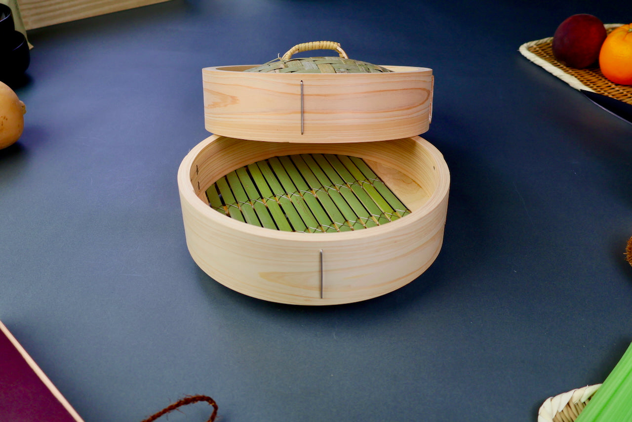 thick wood round bamboo steamer set woven top with loop natural wood tone with printed hiragana surrounded by japanese kitchenware blue gray background