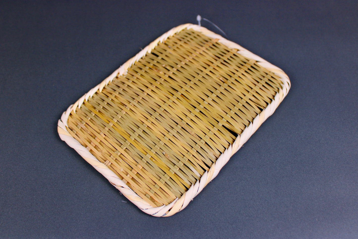 woven bamboo strainer rectangular tan brownish in color in grey blue backdrop