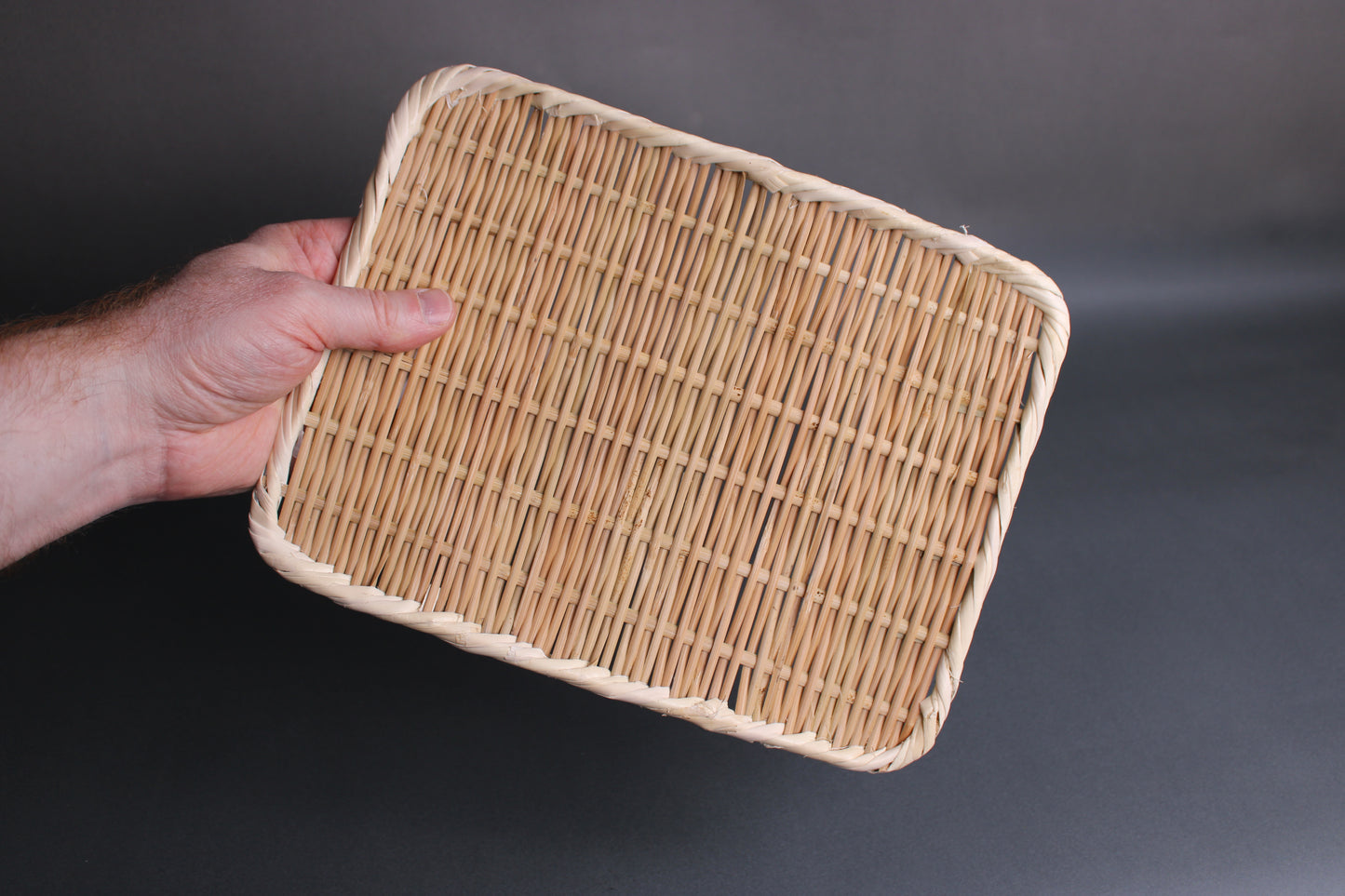 hand holding 21cm rectangle bamboo plate made in Japan in front of dark grey background