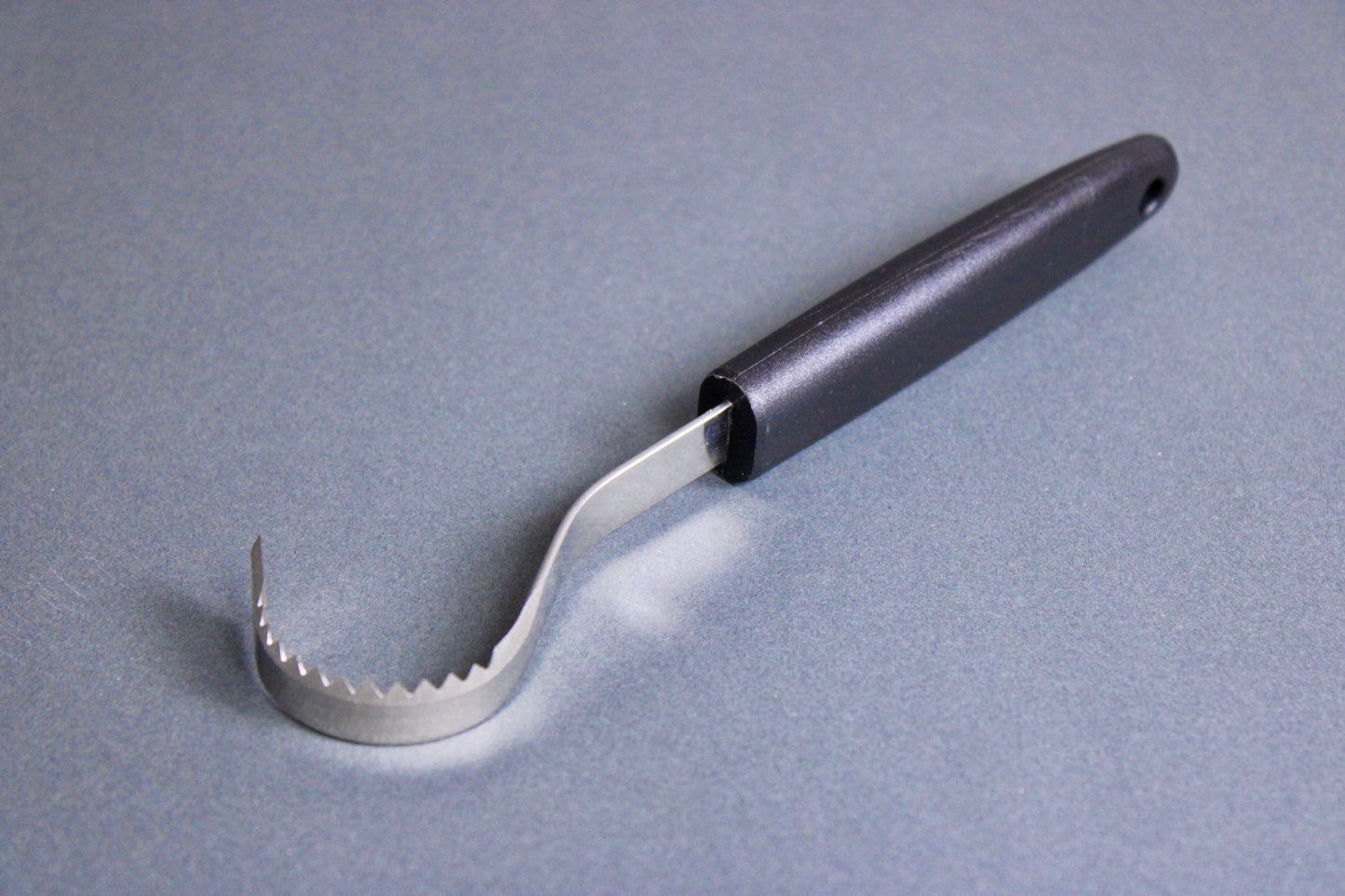 long thin black plastic handled stainless steel curved serrated tool butter curler on grey background