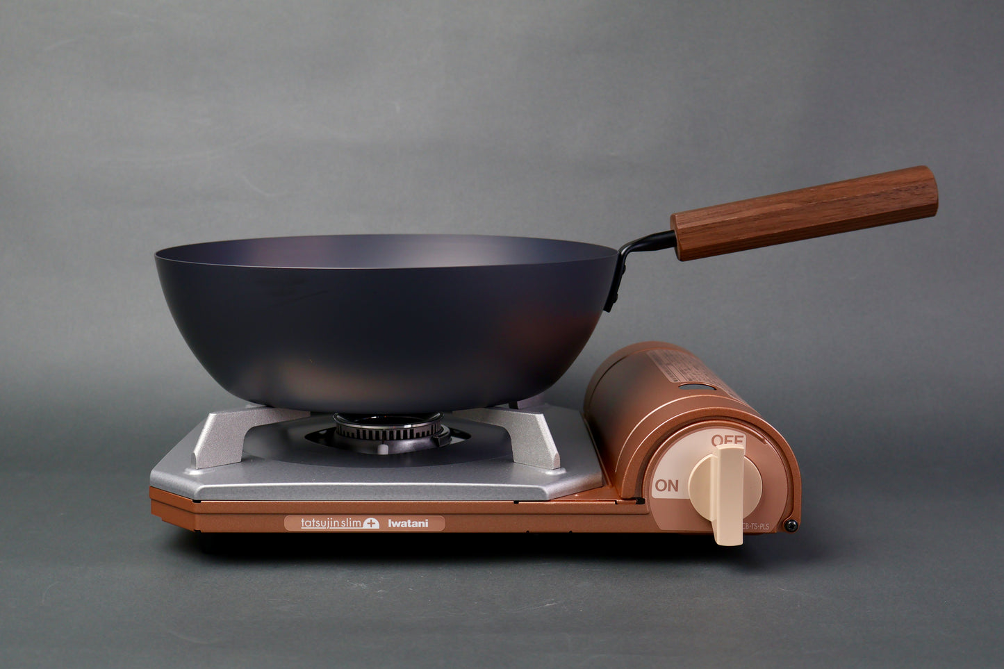 frontal shot of bluish black deep carbon steel pan long wood handle sitting atop tan silver colored portable butane stove