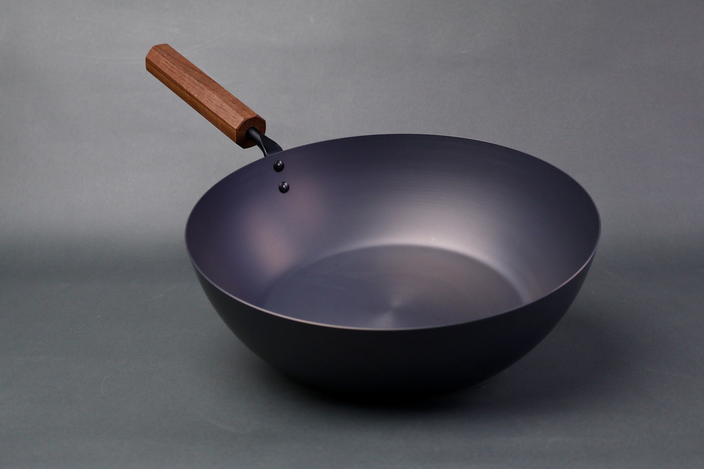 wide deep bluish black carbon steel pan long octagonal wood handle in light grey backdrop