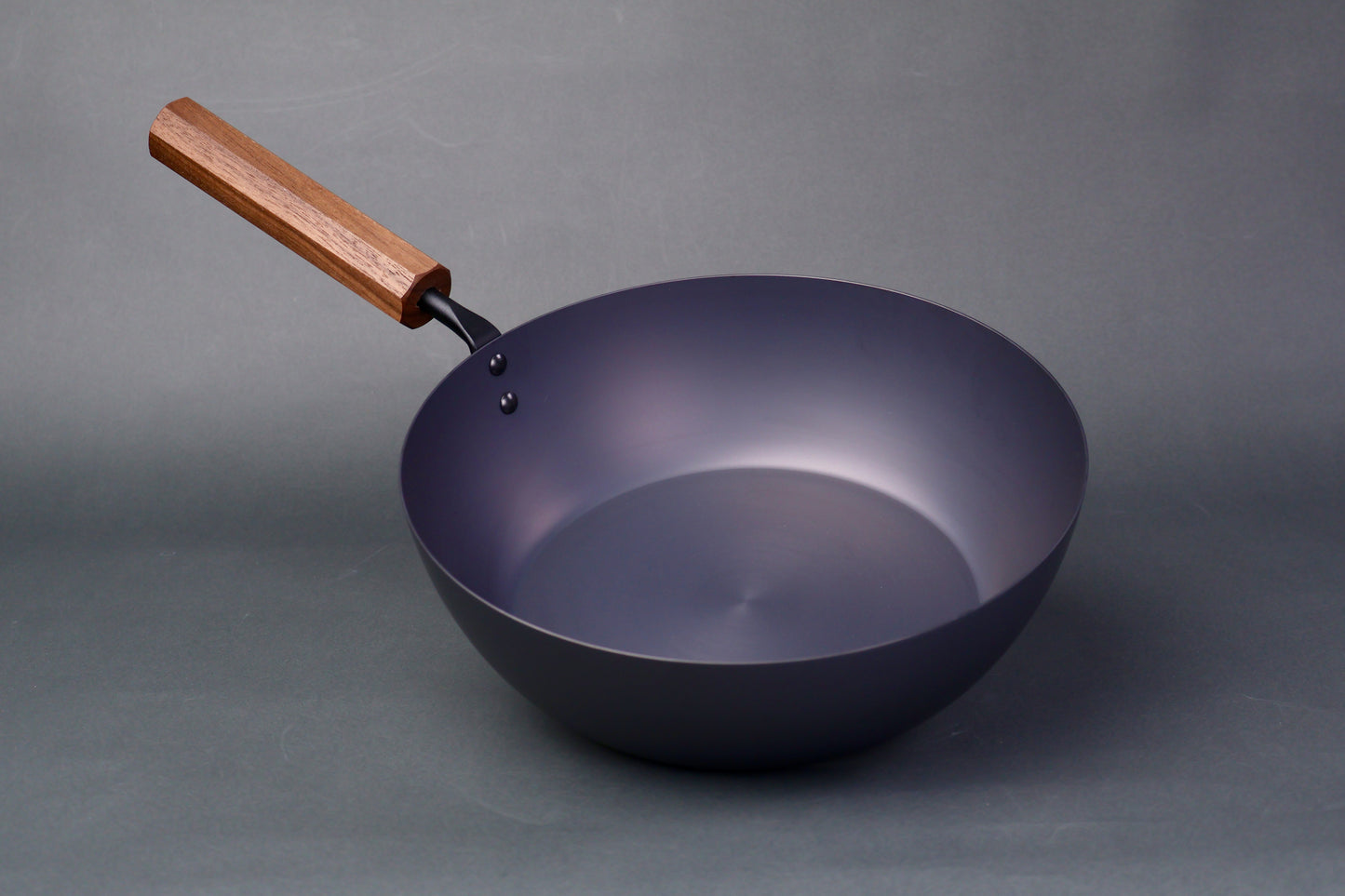wide deep bluish black carbon steel pan long octagonal wood handle in light grey backdrop