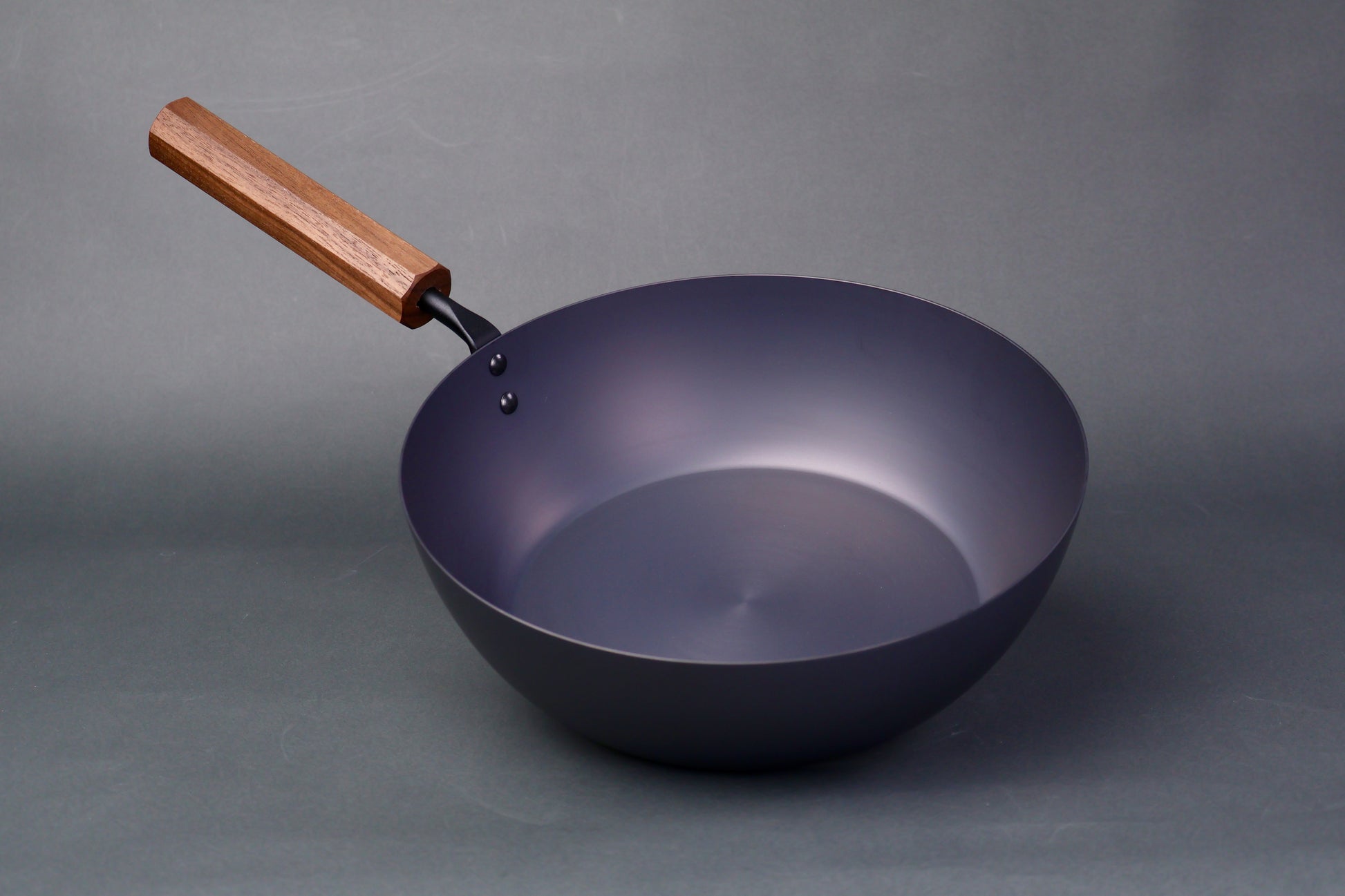 wide deep bluish black carbon steel pan long octagonal wood handle in light grey backdrop