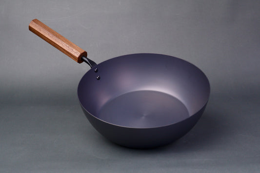 wide deep bluish black carbon steel pan long octagonal wood handle in light grey backdrop