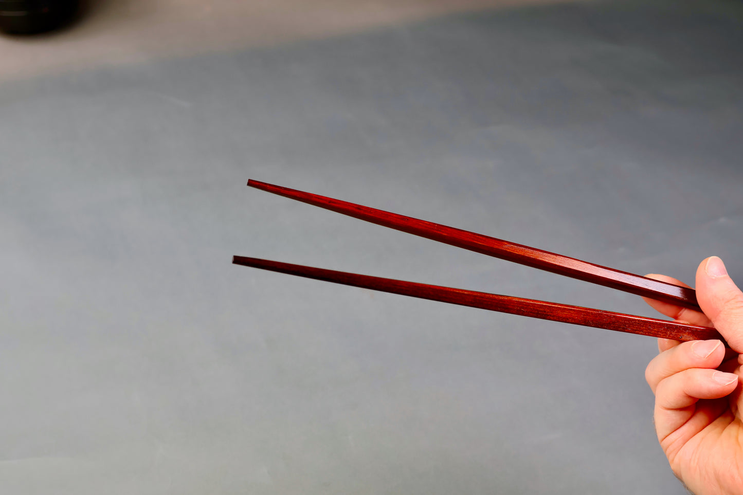 hand holding long square brownish tan hinoki wood cooking chopsticks urushi lacquered connected with white twine grey backdop