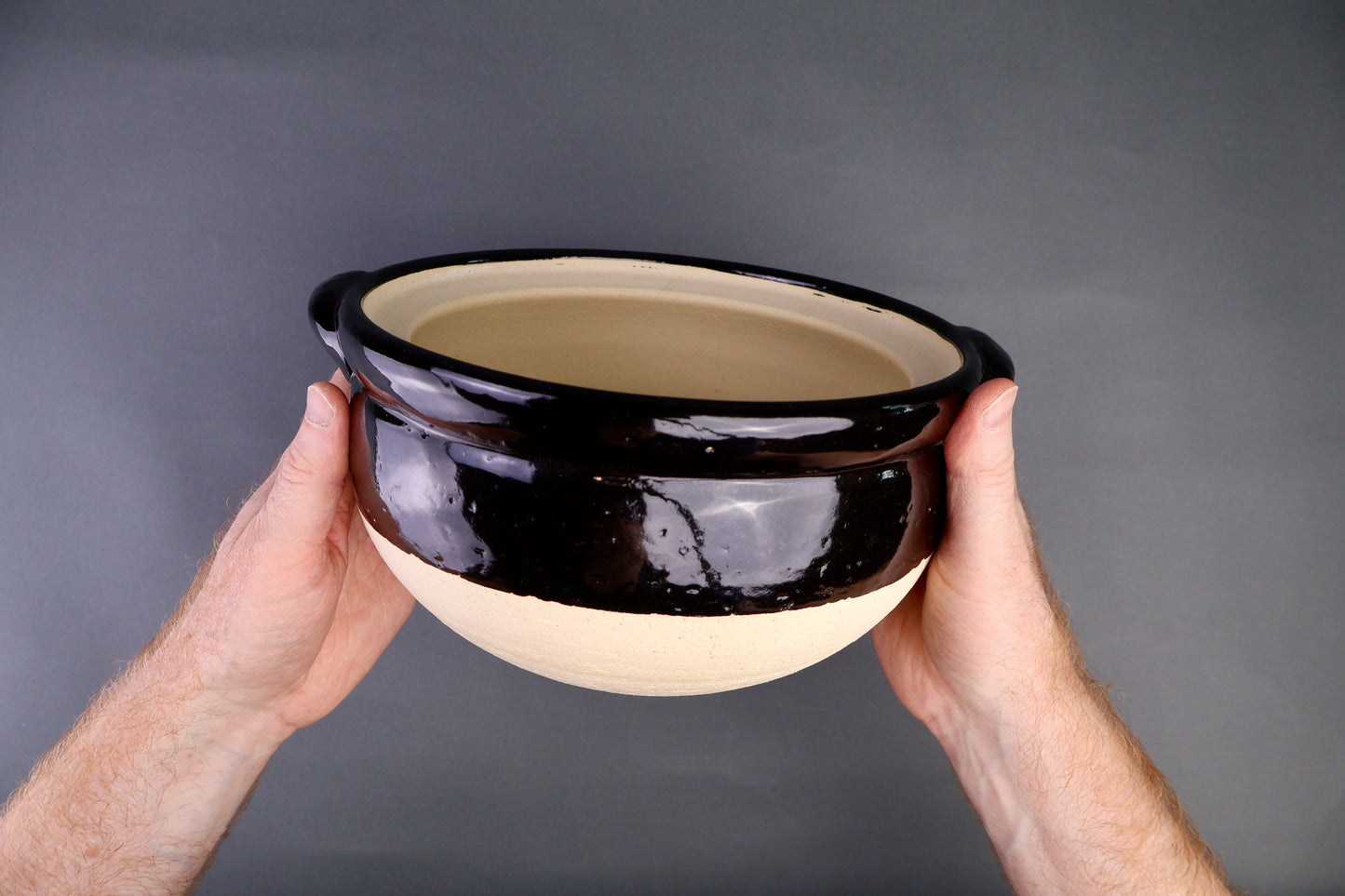 hands holding black glazed donabe rice cooker without main lid showing inner lid glazed black surface in grey background