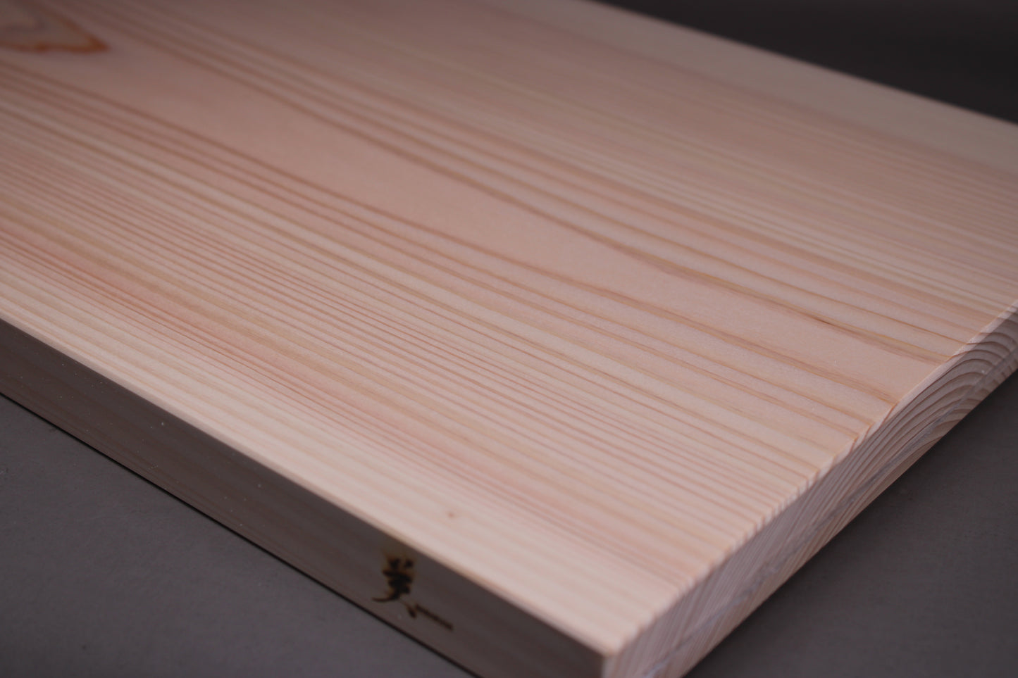 close up of rectangular shaped light medium deep wood tan hinoki cutting board with deep natural grain lines in front of dark grey backdrop