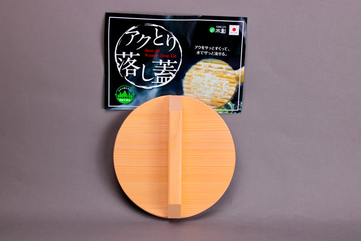 circular wood drop lid with long shallow handle yellowish gold hue beside black product tag with hiragana in front of grey background