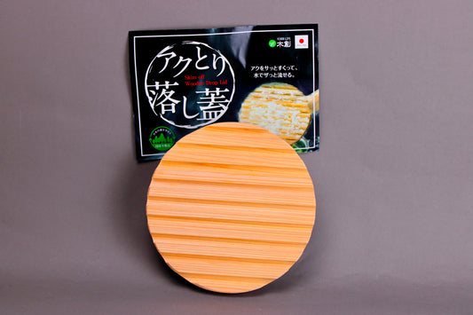 back side with ridges circular wood drop lid with long shallow handle yellowish gold hue beside black product tag with hiragana in front of grey background