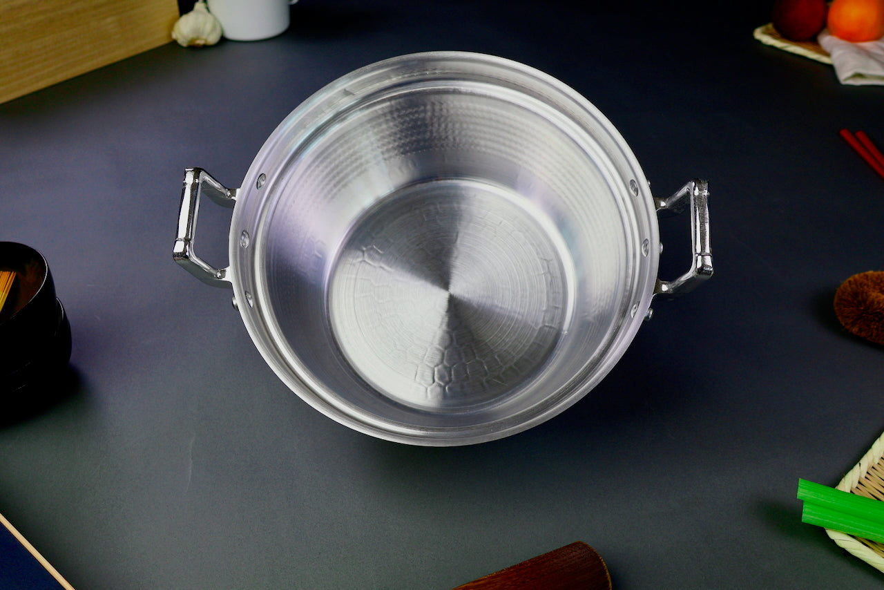 interior of two handled stepped aluminum silvery pot surrounded by japanese kitchenware on a dark grey backdrop
