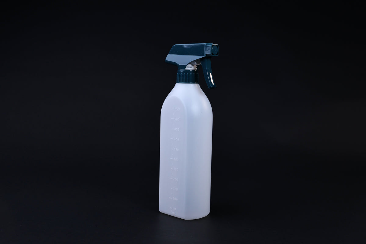 Flat-sided spray bottle standing upright on black background, teal trigger head and embossed volume markings