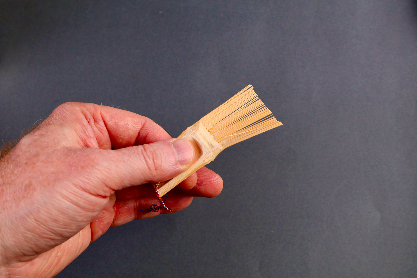 hand holding small bamboo brush thin bristles yellowish tan tone natural bamboo wood on dark grey backdrop