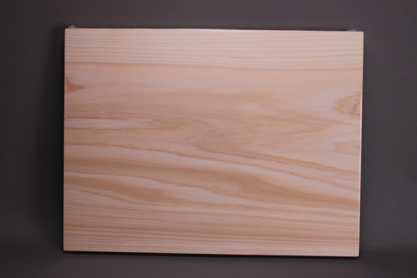 rectangular shaped light medium deep wood tan hinoki cutting board with deep natural grain lines in front of dark grey backdrop