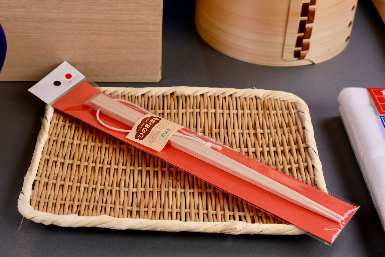 japanese square cooking chopsticks made of hinoki cypress in red package on top of bamboo plate with wood cookware surrounding