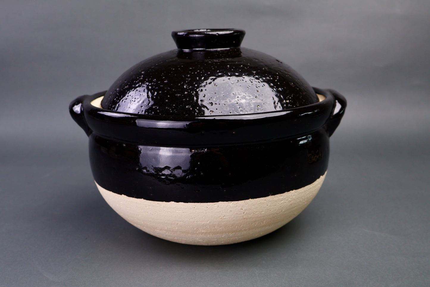 black ceramic handmade donabe rice pot with a two lids on a gray surface