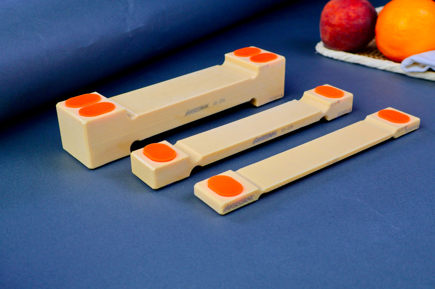 three sizes of hasegawa cutting board lifters long rectangular shaped with pill shaped bright orange oval non slip material in blue grey background with fruit and towel