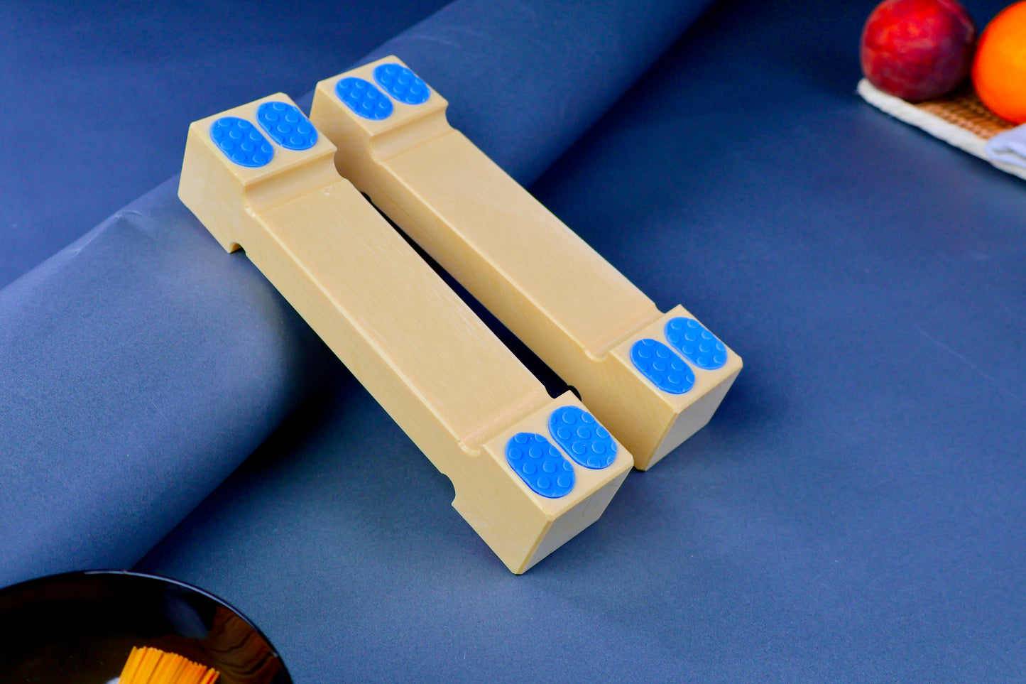 hasegawa cutting board lifter forty five mm tall long rectangular shaped with pill shaped bright blue oval non slip material in blue grey background with fruit and towel