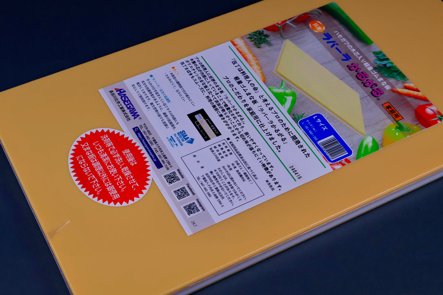 detail of long yellow rectangular shaped rubber cutting board with product paper in hiragana showing bright green red blue images surrounded by kitchenware on grey background