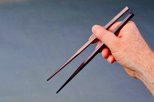 hand holding two urushi coated dark brown chopsticks in light grey background