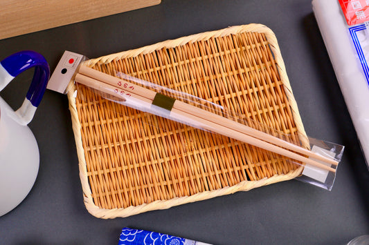 long round hinoki wood chopsticks on rectangular yellowish bamboo plate surrounded by kitchenware dark grey backdrop