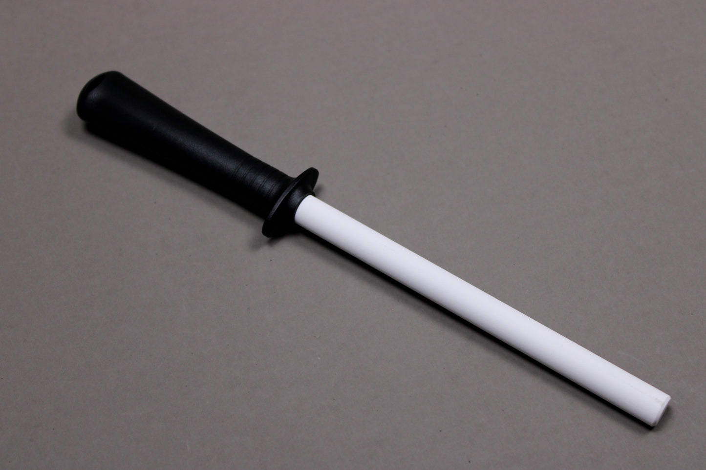 plastic black handled white ceramic honing rod angled on grey background