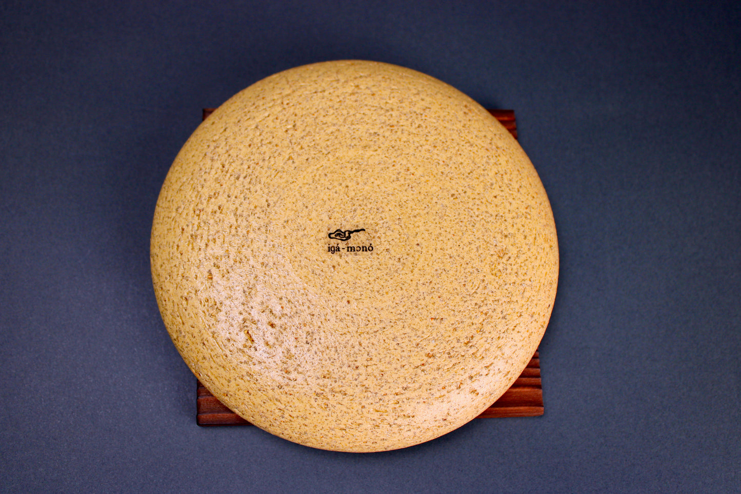 round yellowish ceramic lid sitting atop tan wood trivet in grey background