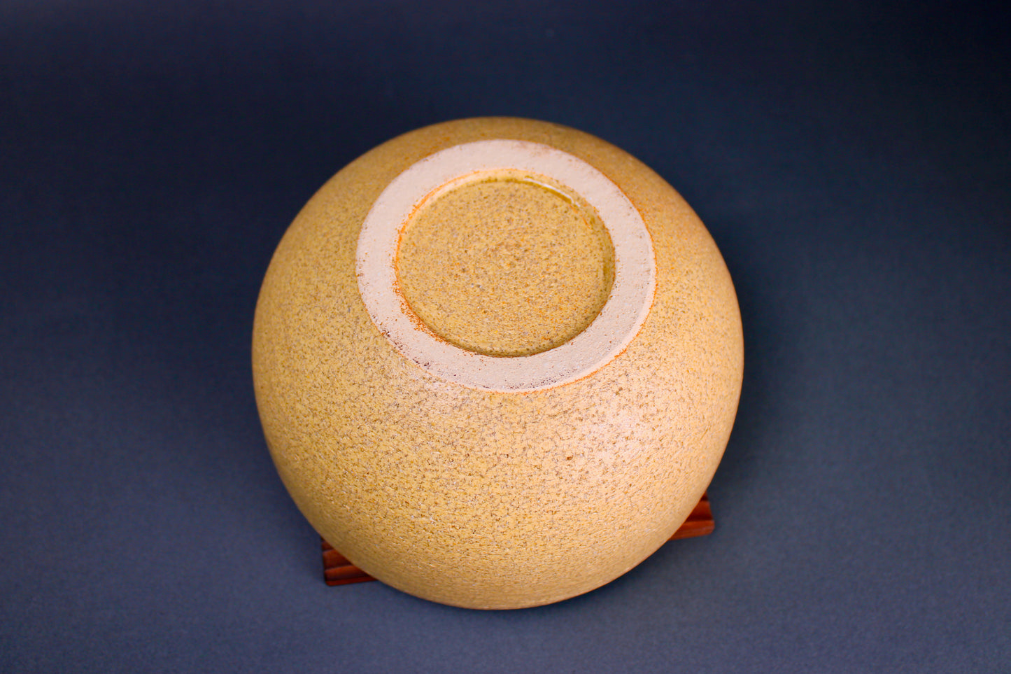 round yellowish ceramic bowl underside sitting atop tan square wooden trivet in grey background