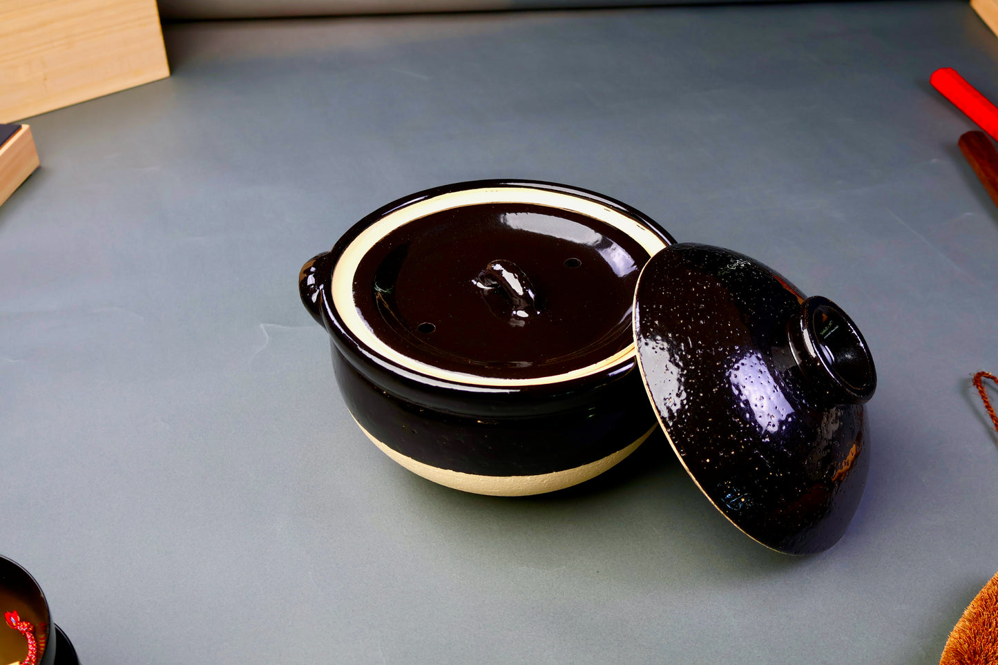 black glazed ceramic rice donabe with two lids surrounded by grey background