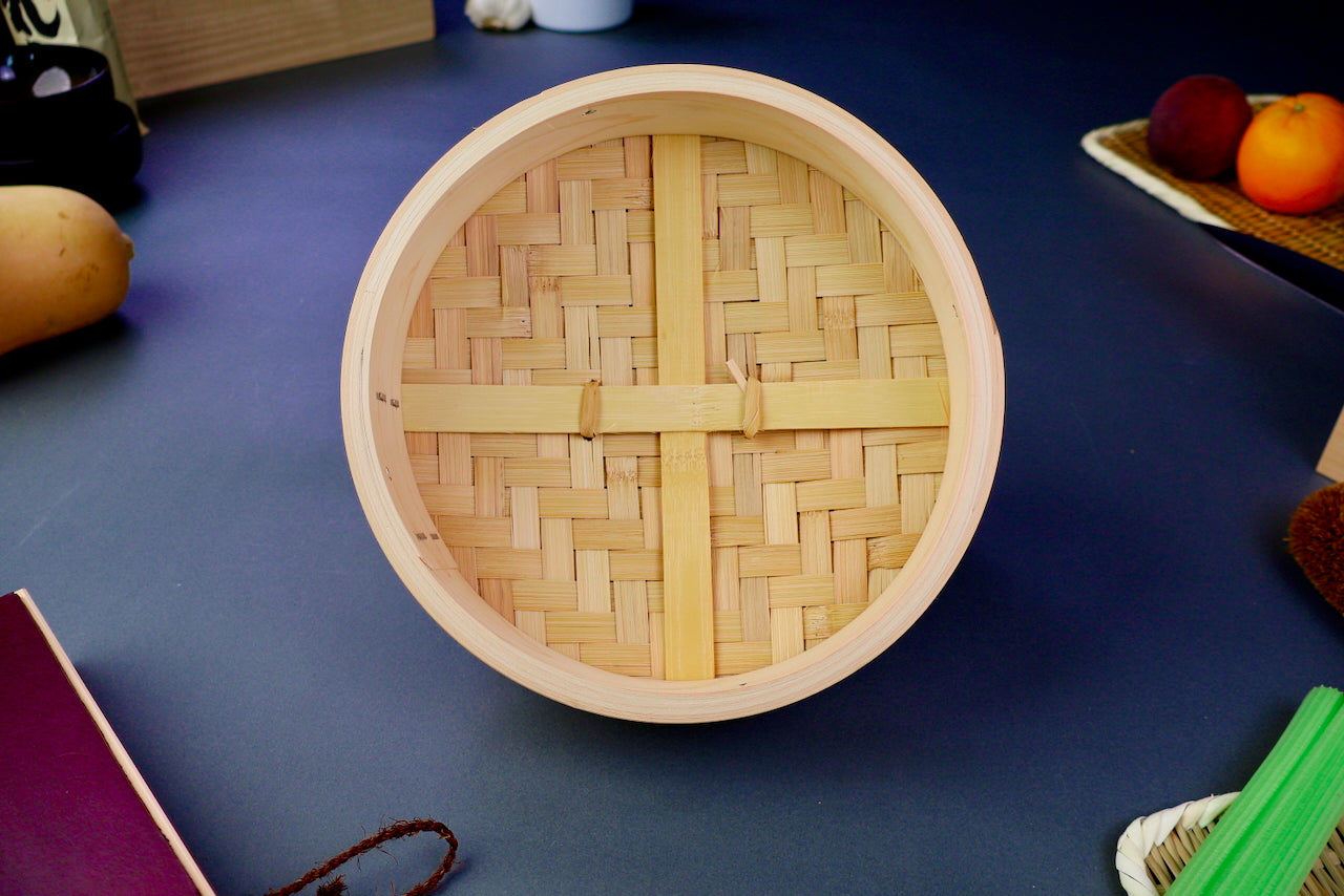 round thick lid of bamboo steamer interior showing three support slats and woven bamboo top surrounded by kitchenware on blue gray surface