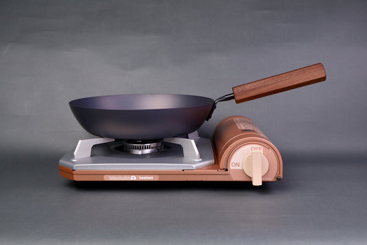 wide low bluish grey black carbon steel saute pan octagonal wood handle sits atop portable butane stove in grey background