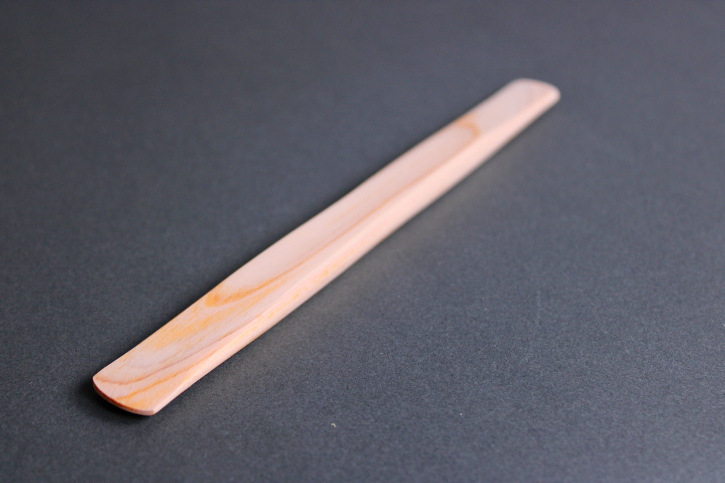 long thin flat natural wood tone hinoki spreader in dark grey backdrop