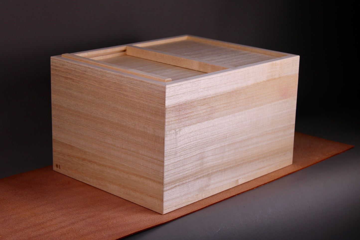 tall rectangular paulownia wood rice box sliding door on top sitting on dark brown leather surface dark grey background