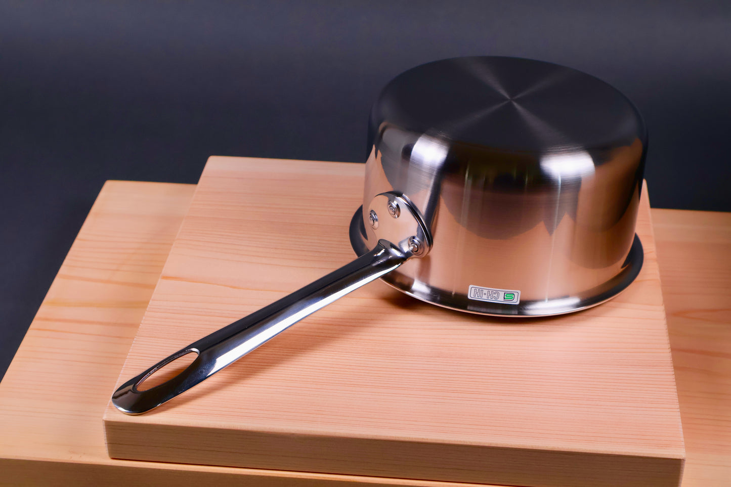 japanese steel saucepan made in Niigata underside showing shiny surface atop wood boards with dark grey background