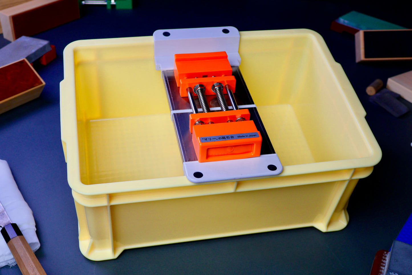 tall yellow box holding whetstone bridge and rubber holder orange color surrounded by knife sharpening accessories in dark background