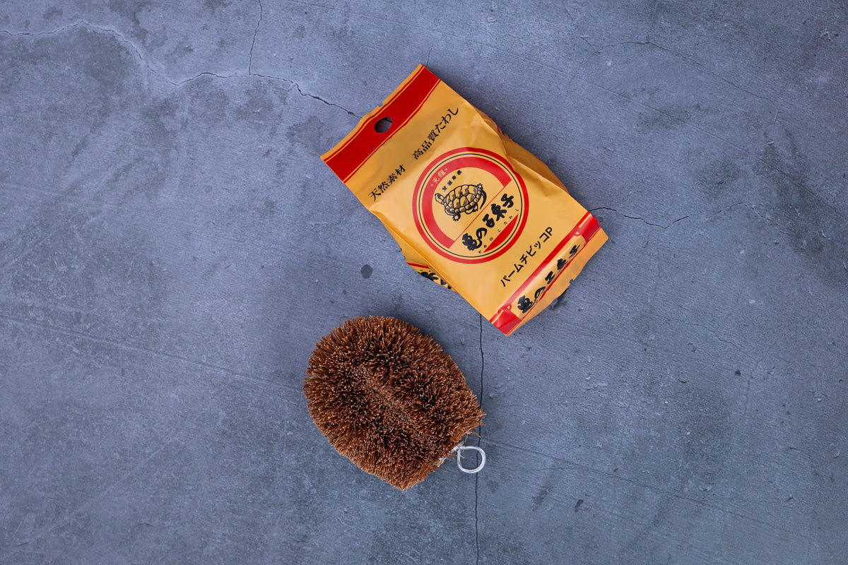 Kamenoko Tawashi palm-size scrub brush — brush and original Japanese packaging flat lay