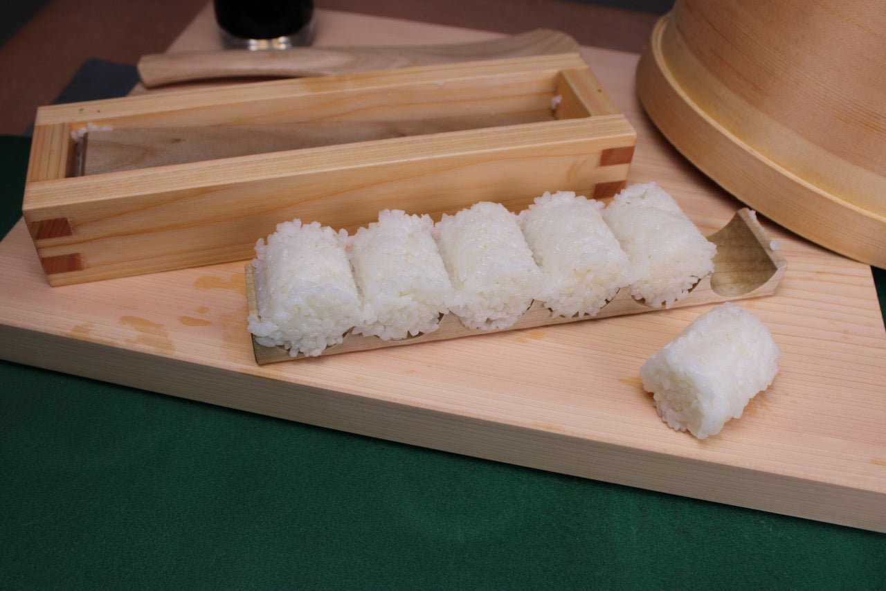 yamacoh bale shaped onigiri maker with barrel shaped prepared rice with kitchen backdrop