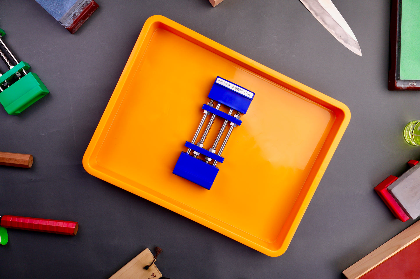 yellow orange colored short plastic knife sharpening box with rubber plastic whetstone holder blue inside surrounded by knife sharpening items grey surface