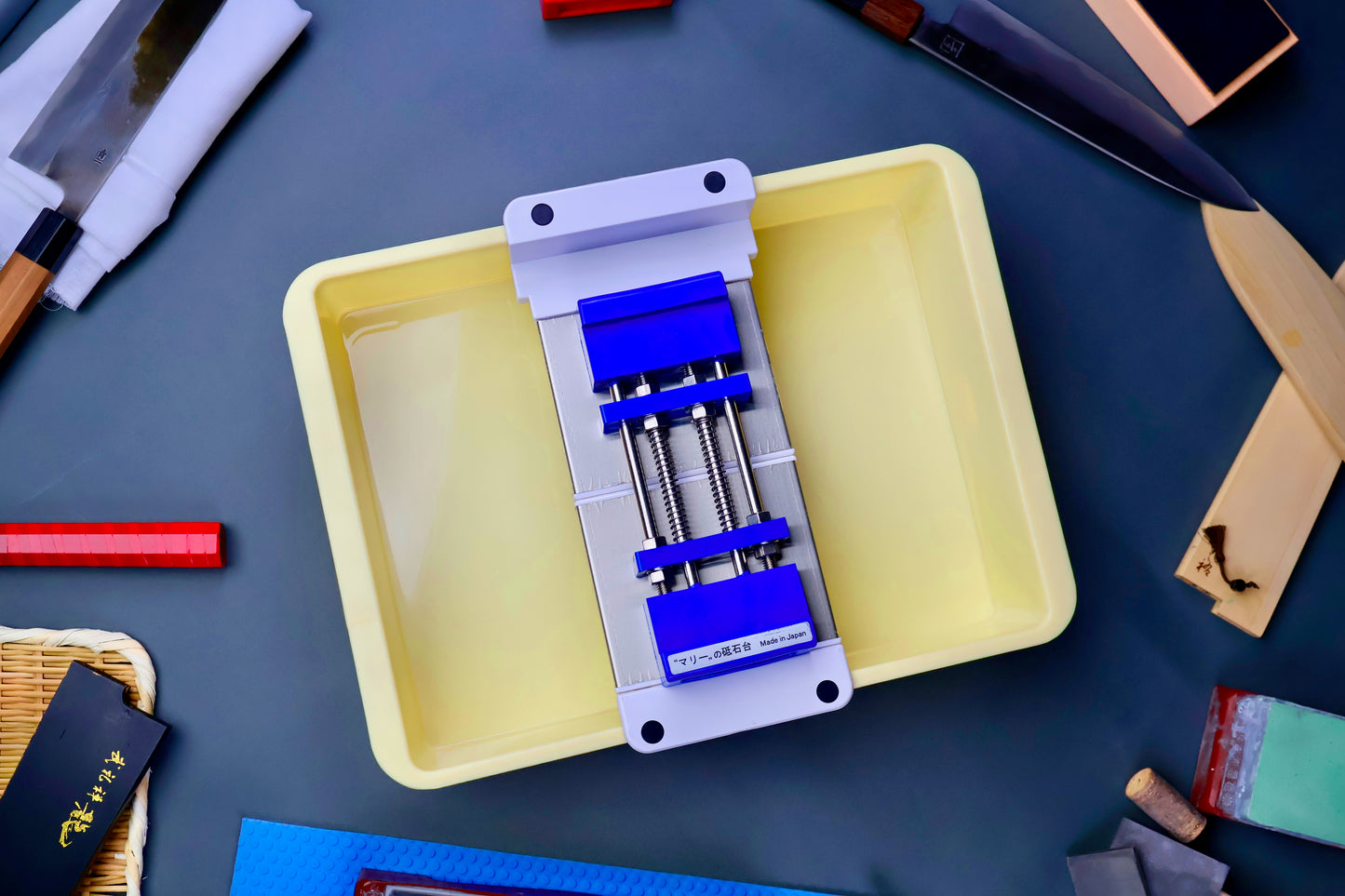 top down shot of short yellow box holding suehiro multi sliding rack marie whetstone holder blue surrounded by japanese knife accessories