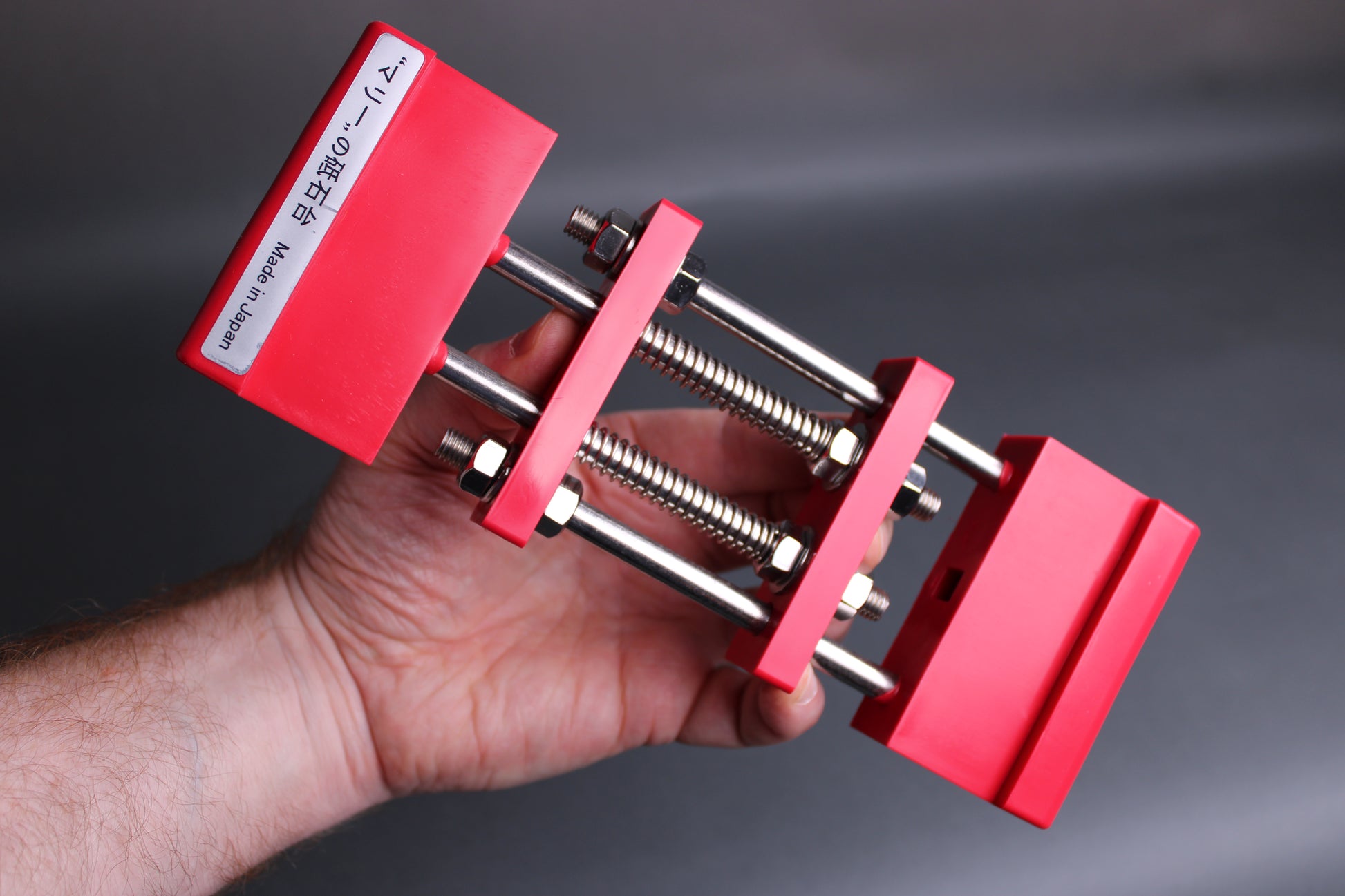hand holding red whetstone holder rectangle shape springs rods dark background
