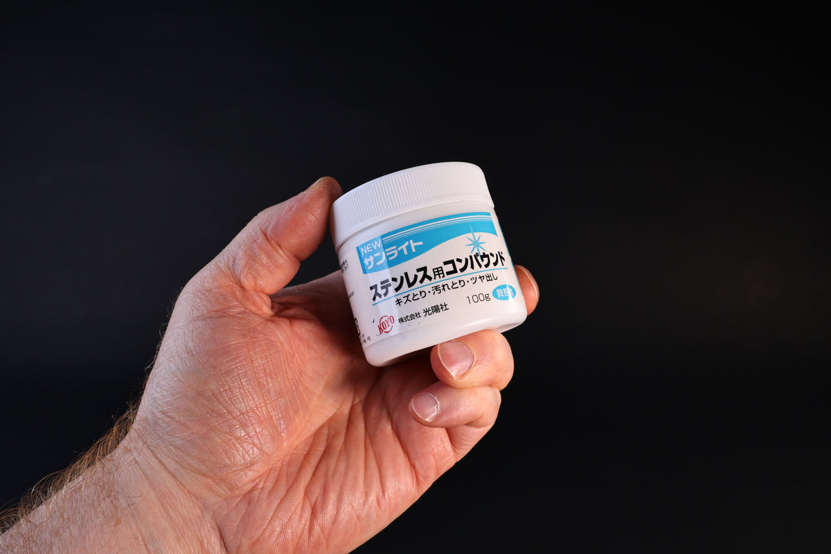 Koyo New Sunlite stainless steel polishing compound in a 100g white jar with blue label, held against a dark background