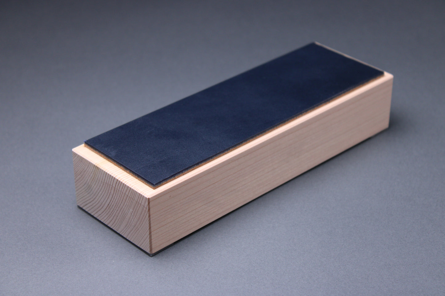 english bridle leather knife strop colored midnight blue mounted to tall hinoki wood yoshino base with smooth sides showing tree rings with light grey background profile shot