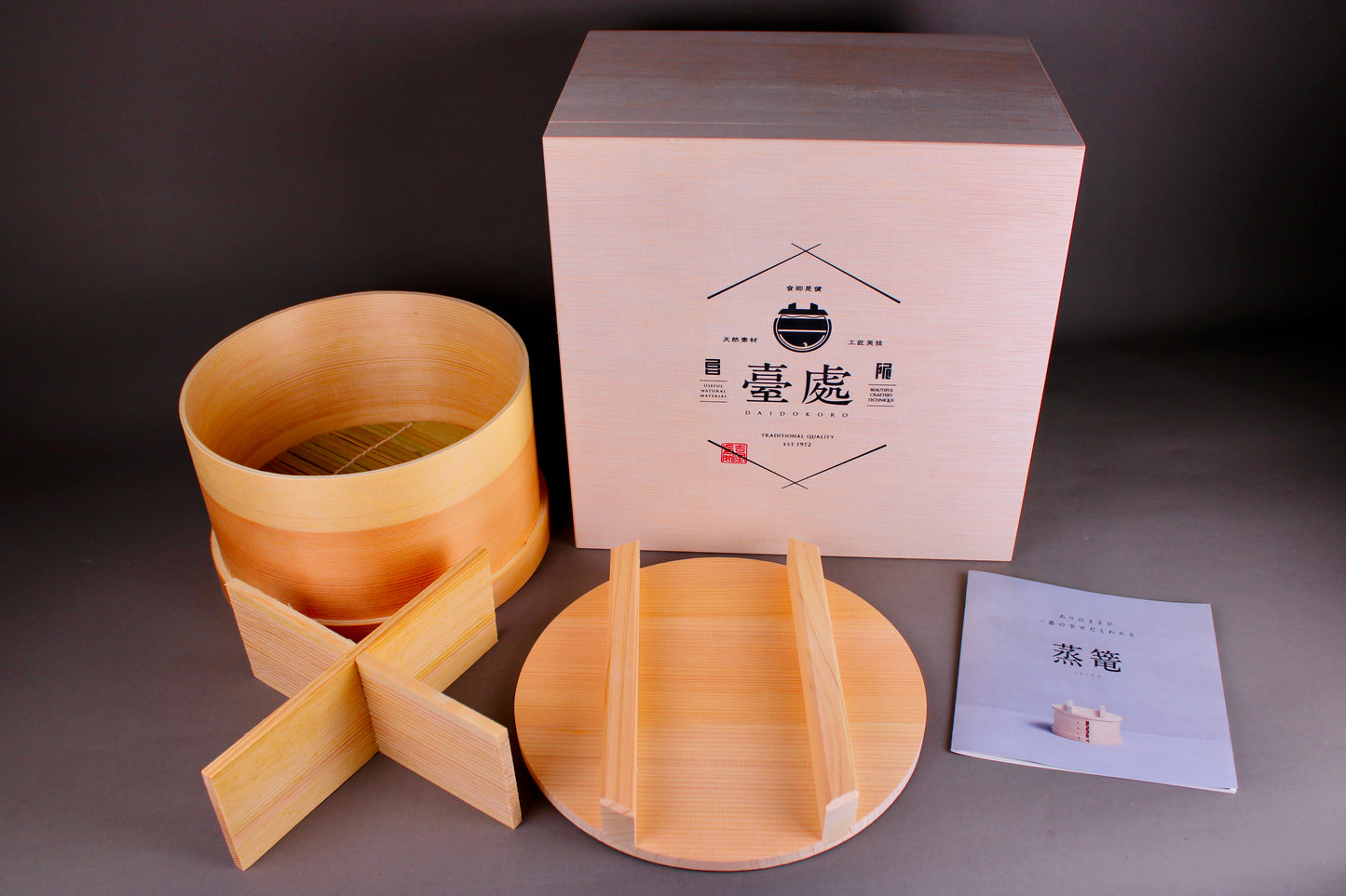 disassembled japanese steamer set with round wood body large pale wood gift box divider insert wide round lid paper pamphlet with kanji writing all on dark gray surface