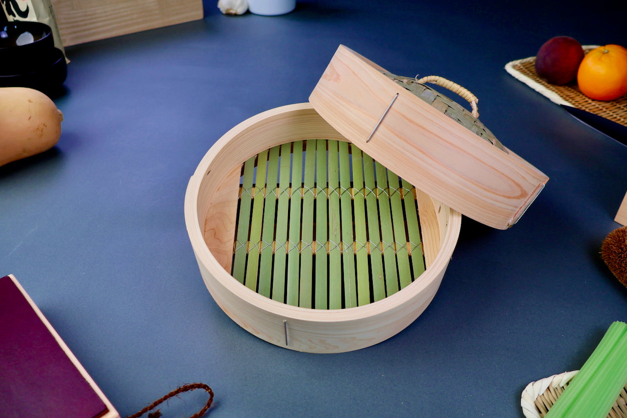 thick wood round bamboo steamer set woven top with loop natural wood tone with printed hiragana surrounded by japanese kitchenware blue gray background